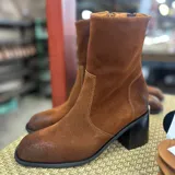 Bota corta de cuero vacuno color marrón oscuro, con taco cuadrado de madera y punta cuadrada. Presenta un diseño minimalista con cierre lateral interno y caña con elástico.