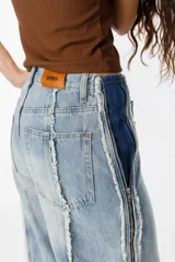 Jean de corte recto y tiro medio, confeccionado en denim de algodón en tono azul claro. Presenta un diseño distintivo con cierres laterales a lo largo de las piernas y detalles de costuras desflecadas.