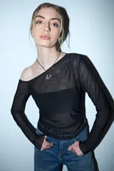Remera de manga larga y escote asimétrico, confeccionada en tul negro transparente. Lleva un top negro opaco debajo y un cinturón de cadena plateada a la altura de la cadera.