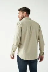 Camisa de hombre color beige con efecto stone wash, corte regular, cuello clásico, cierre frontal con botones, dos bolsillos con solapa abotonada en el pecho y mangas largas con puños abotonados.