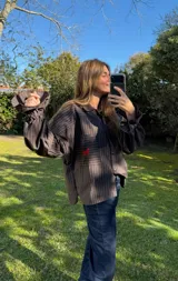 Camisa oversize a rayas marrón y negro, con cuello camisero, bolsillo frontal grande con bordado rojo de un caballo, y mangas abullonadas con puños elásticos.