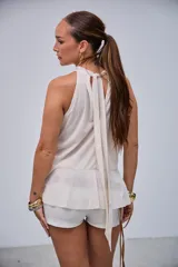Blusa sin mangas de color crudo con cuello halter y abundantes volados en la parte frontal y sisas.
