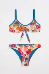 Conjunto de bikini con estampado multicolor sobre fondo celeste, con diseño de flores, macetas y un camello. El corpiño tiene escote en V con nudo delantero y tirantes regulables azules, y la bombacha es de tiro bajo tipo vedetina.