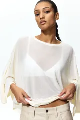 Top de corte holgado en punto transparente, color beige, con mangas murciélago tres cuartos, escote redondo y bajo recto.