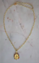 Cadena dorada con dije ovalado de la Virgen María en baño de oro, rodeado de pequeños cristales de colores variados.