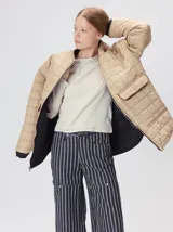 Campera reversible capitoneada con cierre frontal. Un lado es de color negro y el otro es de color beige, ambos con diseño acolchado. Cuenta con cuello redondo, mangas largas y bolsillos laterales.