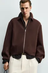 Cazadora boxy fit marrón de corte corto, confeccionada en tejido con mezcla de lana. Presenta cuello camisero, cierre frontal de cremallera metálica, bolsillos de vivo en la cadera y mangas largas.