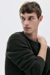 Buzo de punto acanalado color verde oscuro, de manga larga y cuello redondo, con corte regular fit.