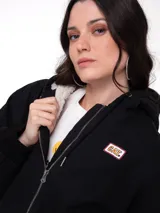 Chaqueta negra de lona con forro interior de sherpa, cierre frontal con cremallera, capucha ajustable con cordón y puños y bajo de punto acanalado.