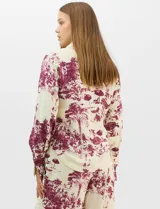 Conjunto de dos piezas compuesto por camisa de manga larga con cuello solapa y botones frontales, y pantalón de tiro alto con pierna recta y bolsillos laterales. Ambas prendas presentan un estampado paisajístico en tonos marrones sobre fondo crema.