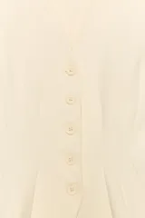 Chaleco color beige confeccionado en tejido de punto elástico, con escote en V, sin mangas y bajo acabado en línea evasé con cierre frontal de botones.