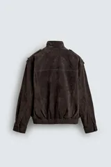 Cazadora de corte relajado confeccionada en piel con acabado de ante. Presenta cuello subido, cierre frontal de cremallera oculta por solapa con botones a presión, bolsillos de plastrón con solapa en el pecho y bolsillos de vivo en la cadera. Incluye trabillas en los hombros, mangas largas con puños abotonados y bajo con elástico.