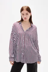 Camisa de corte holgado con estampado de rayas verticales en tonos bordó y blanco. Presenta cuello clásico, cierre frontal con botones, mangas largas con puños abotonados y un bolsillo frontal en el pecho.