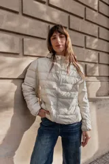 Campera puffer ultraliviana color beige, con diseño acolchado horizontal, capucha incorporada, cierre frontal y bolsillos laterales.