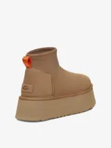 Bota corta tipo botineta de la marca UGG, color negro, con diseño de caña baja y plataforma elevada. Presenta una tira de agarre en color amarillo neón en la parte posterior y una suela de goma gruesa con textura acanalada.