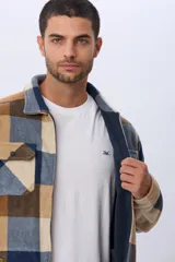 Campera leñadora de tejido polar con estampado a cuadros en tonos marrones, beige y azules. Presenta cierre frontal, cuello camisero, bolsillos superiores con solapa y bolsillos laterales.