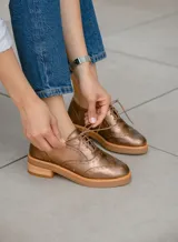 Zapato acordonado estilo oxford de cuero vacuno en color plateado metalizado, con diseño brogue, suela de goma y taco de madera.