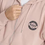 Campera con cierre frontal y capucha, color beige, con logo circular de la marca Reef estampado en el pecho y bolsillos tipo canguro.
