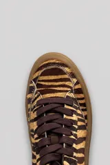 Championes urbanos de cuero con estampa animal print tipo tigre en tonos marrones y beige. Tienen suela de goma marrón y cordones al tono.