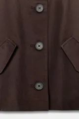 Chaqueta corta de color marrón oscuro, con cuello de solapa, manga larga con trabillas en los puños, bolsillos delanteros con solapa y cierre frontal con botones.