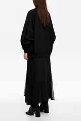 Vestido largo de estilo casual, confeccionado en tejido tipo sudadera color negro. Presenta cuello redondo, mangas largas con detalles de remaches metálicos en los hombros y brazos, y una falda plisada de corte amplio.