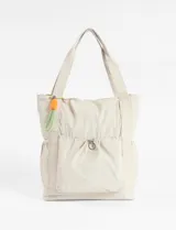 Bolso versátil color natural, convertible en mochila o cartera shopper. Cuenta con un bolsillo frontal con cierre de cordón elástico y un detalle decorativo colgante en colores vibrantes.