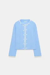Chaqueta de popelín a rayas celestes y blancas, con cuello redondo y mangas largas. Presenta detalles de encaje a contraste en el cuello, los puños y la botonadura frontal, la cual cuenta con cierre de botones.