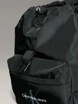 Mochila negra de Calvin Klein Jeans, modelo Sport Essentials Flap, confeccionada en poliéster reciclado. Tiene cierre elástico con broche en la solapa, asas ajustables, bolsillo exterior con cierre y logo de la marca.