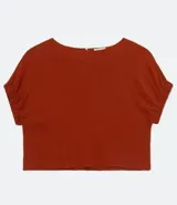 Blusa color ladrillo de tejido viscolino, con escote redondo, manga corta abullonada con elástico en el dobladillo y abertura en gota en la espalda con cierre con botón.