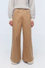 Pantalón de vestir color crema, de corte ancho y tiro alto. Se ajusta a la cintura con cinturón de cuero marrón.