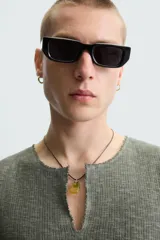 Camiseta sin mangas de punto acanalado, color verde oliva desgastado, con cuello redondo y abertura frontal en forma de 'V'. Presenta un estampado desvanecido en el centro del pecho.