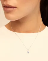 Charm de metal con baño de oro y cristal azul engastado en el centro, diseñado con una forma redonda y argolla superior para colgar.