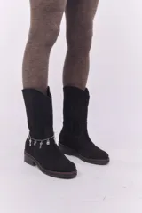 Bota de caña media confeccionada en cuero gamuzado color negro, con costuras a la vista en tono contrastante. Presenta un detalle de cadena metálica plateada con dijes colgantes en forma de llaves y candados alrededor del tobillo. Cuenta con un taco cuadrado de madera y suela de goma.