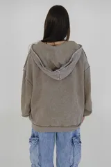 Canguro con cierre frontal, confeccionado en tela con efecto desgastado color beige. Presenta costuras expuestas, diseño holgado, capucha y un pequeño bordado de estrellas en el frente.