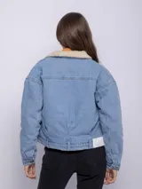 Campera de jean blanca con interior de corderito color beige, dos bolsillos grandes en la parte frontal y siete botones metálicos.