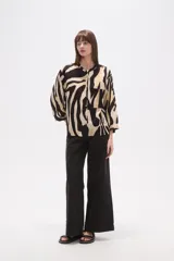Camisa de corte holgado con estampado animal print tipo cebra en tonos negro y beige. Presenta cuello mao, cierre frontal con botones y un bolsillo aplicado en el pecho.