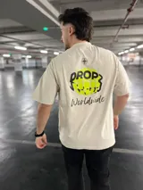 Remera negra con efecto washed, con estampado trasero de un globo terráqueo en verde vibrante y la palabra "Dropz" en blanco. Debajo, la palabra "Worldwide" en tipografía script blanca y un símbolo de brújula en la parte superior.