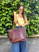Bolso grande de cuero marrón, tipo shopper, con costuras artesanales decorativas en contraste a lo largo del borde superior y las asas de hombro.