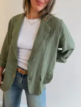Blazer de lino color verde militar, con cuello de solapas, cierre frontal de dos botones y bolsillos frontales tipo ojal. Diseño de corte relajado y mangas largas.