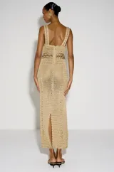 Vestido largo dorado de crochet con diseño artesanal y textura abierta, tirantes anchos y detalles de cordones cruzados en el escote y la cintura.
