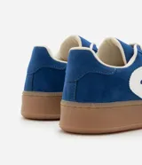 Championes deportivos de mujer modelo chuteira, color azul con aplique lateral en forma de 'V' blanca. Presenta capellada de gamuza sintética, cordones blancos y suela gruesa de goma color caramelo.