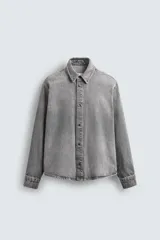 Camisa de corte relajado confeccionada en denim de algodón con efecto lavado. Presenta cuello solapa, cierre frontal con botones y mangas largas con puños abotonados.