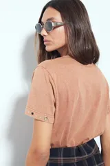 Remera de manga corta color marrón con escote a la base y calce relajado. Las mangas presentan terminación con ojales metálicos.