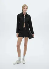 Chaqueta negra de corte recto con cuello camisero y cierre frontal de cremallera doble metálica. Presenta diseño de manga larga y estructura entallada.