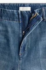 Jean de denim de algodón rígido, color azul con efecto lavado, de tiro alto y corte recto holgado. Cuenta con bolsillos al bies y pliegues marcados al frente y en la espalda.