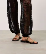 Sandalias planas estilo mule marrones, confeccionadas en PU, con diseño de dedo, dos tiras finas decoradas con aplicaciones de resina y detalles metálicos dorados.