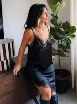 Vestido lencero de satén color blanco con detalles de encaje negro en el escote y el ruedo asimétrico. Presenta breteles finos y un corte fluido que se ajusta suavemente a la silueta.