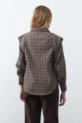 Camisa de manga larga con estampado de cuadros en tonos marrones, azules y amarillos. Presenta cuello clásico, cierre frontal con botones y hombros con estructura levemente marcada.