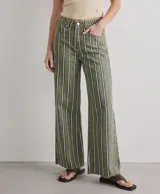 Jean de corte flare y tiro alto, confeccionado en denim verde militar con diseño de rayas verticales blancas y azules, estilo de pernera ancha y bajo deshilachado.