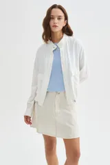 Chaqueta bomber blanca de algodón con cuello mao, bordado sutil, bolsillos frontales con solapa, cierre de botones y cordón ajustable en el ruedo.